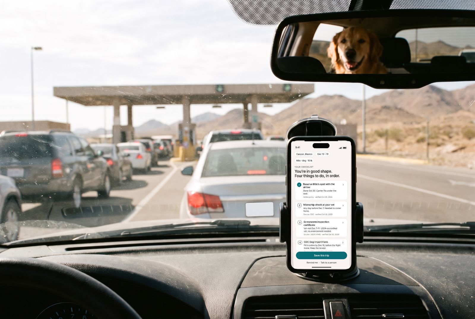 A phone on a car dashboard shows the trip checklist while waiting in the US–Mexico border line, a golden retriever in the mirror